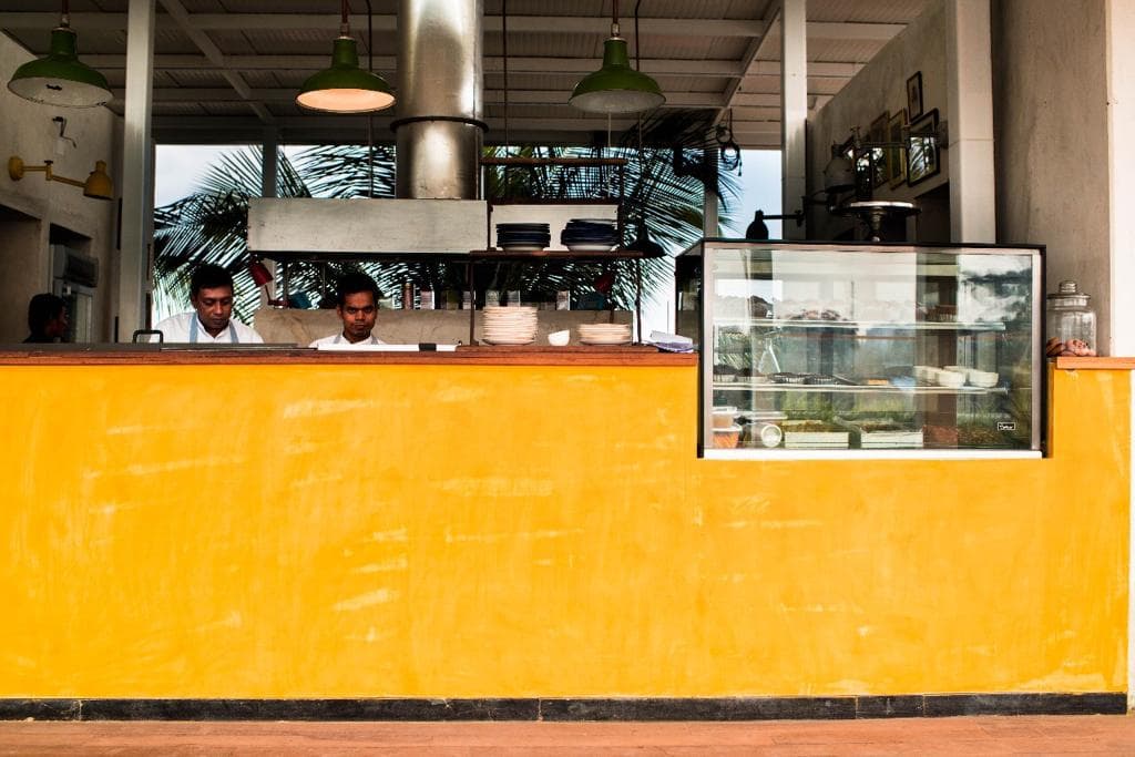 Bright yellow service counter and open kitchen on the Love OORU rooftop with green pendant lights.